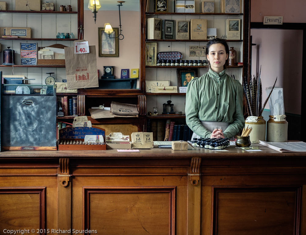 Portrait Photography - Portrait Photographer - colour portrait image of the victorian post mistress standing behind her counter in the victorian shop at the Black country museum