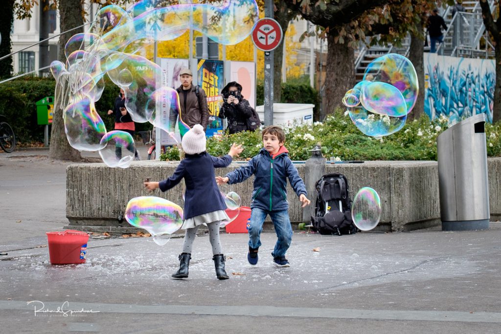 travel photography - travel photograher - images from a visit to zurich this featuring two children enjoying the fun of chasing large bubbles in a park