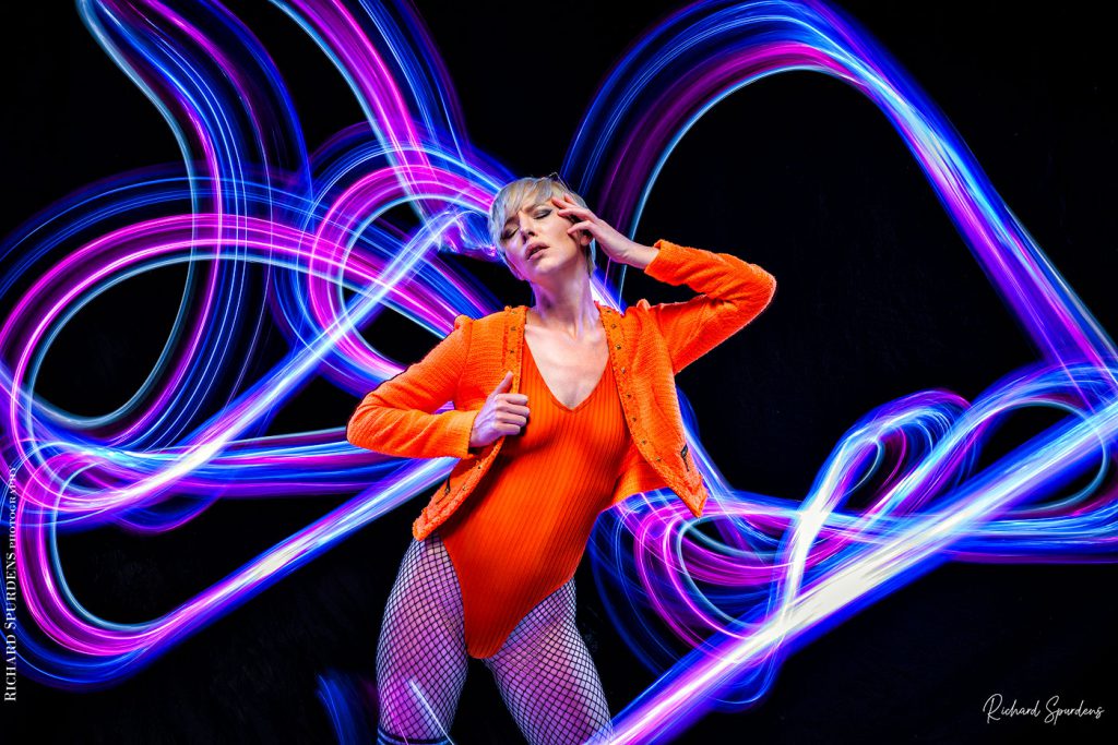 Light painting Photography - Fashion Photographer - colour image of model wearing orange jackets and body lighting swirls around the model using blues and purple lights wands around the model