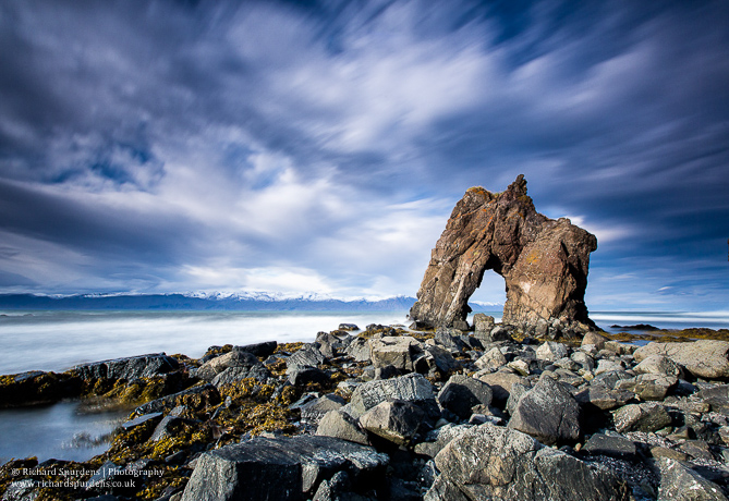 Landscape Photograher - Landscape Photography - colour image of one of the many rock arch around the coast of iceland taken on a windy day so it shows the cloud movement in the sky