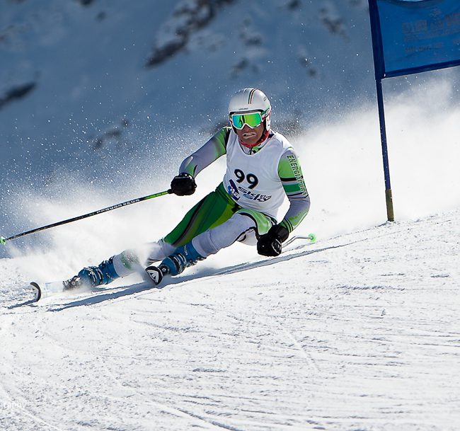 sport photography - sport photographer - a down hill racer standing hard on the edges of his skis as he rounds a blue gate on a demanding giant slalom course in pila italy - skiing action