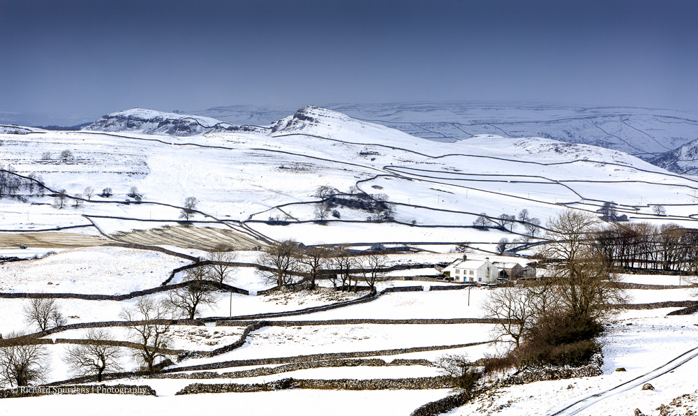 Landscape Photograher - Landscape Photography - colour image of a snow dale a white farm house is on the right hand side third and the dry stone wall patterns stand out well against the snow - a day in the dales -8