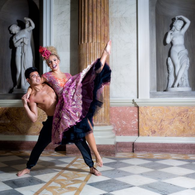 dance photographer - dance photography - colour image of two dancers one male one female the male is performing a side lift of the female as she kicks her top leg into the air. in the background are two roman statues