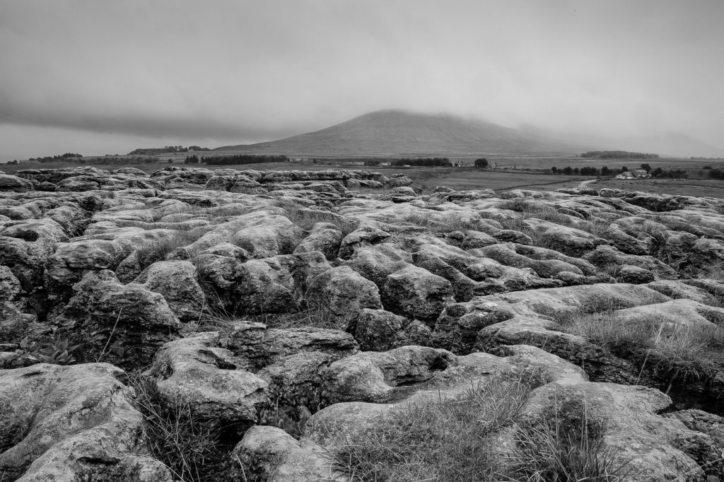 Landscape Photography - Landscape Photographer - monochrome image of the limestone pavement in the foreground with the distant hill top shrouded in the clouds