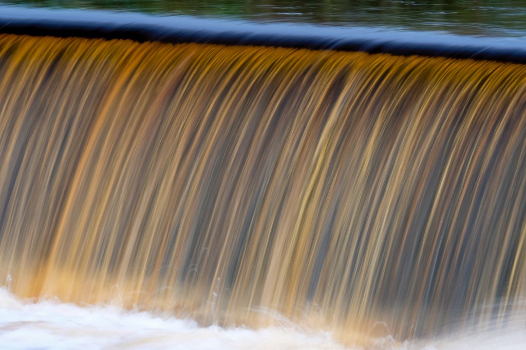 Landscape Photography - Landscape Photographer - colour image of the line of cascading water the colour of Peat flowing down the weir and beyond