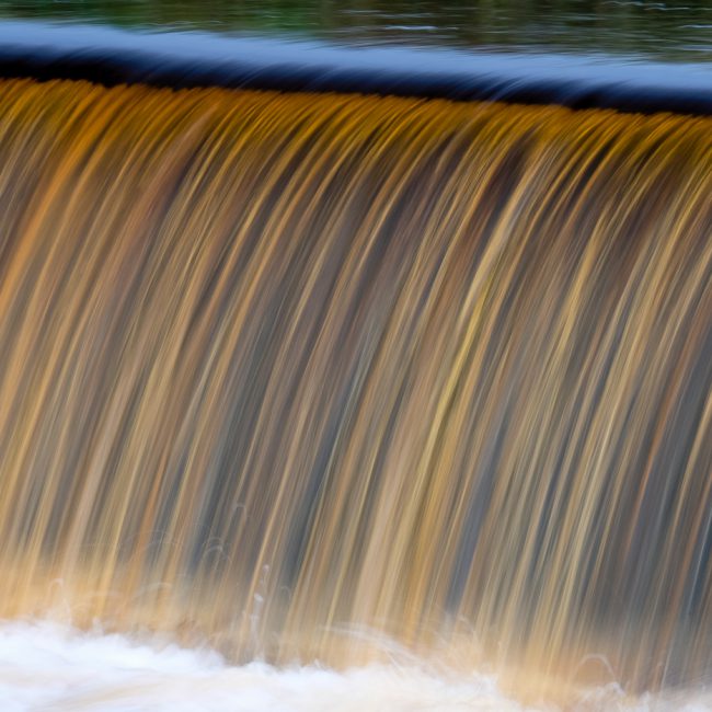 Landscape Photography - Landscape Photographer - colour image of the line of cascading water the colour of Peat flowing down the weir and beyond