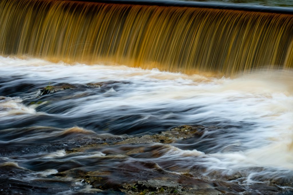 Landscape Photography - Landscape Photographer - colour image of the line of cascading water the colour of Peat flowing down the weir and beyond