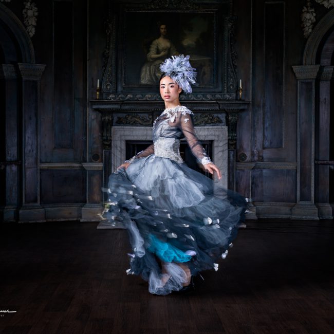 fashion photographer - fashion photography - model in a blue and silver floaty dress she is swirling the skirt to give it movement the colours match the dark room tones