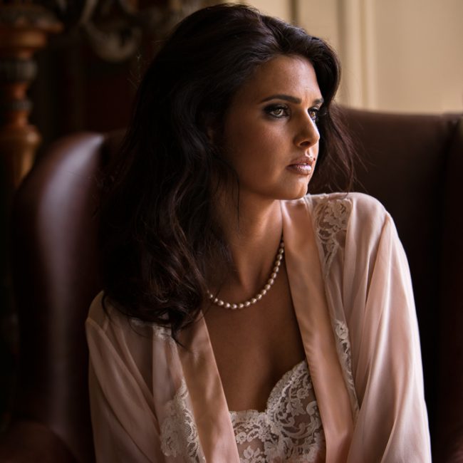 fashion photographer - fashion photography - colour image from a fashion shoot at pipewwll hall featureing designes by Jane-woolrich-design. model is seated in a red winged chair wearing a pink negligee and slip