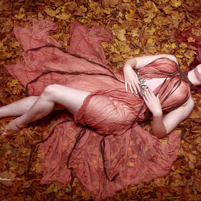 fashion photographer - fashion photography - colour image from shoot with rosewell ivory she is wearing a burnt orange floatly dress and is lying on a bed of autumn leaves she has long red hair and her dress is extended out each side of her