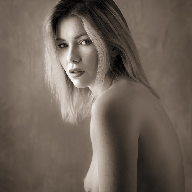 portrait photography - portrait photographer -a toned monochrome image head shot of the model nicky she is look across her shoulder and into the lens the lighting focused on her face and is producing some nice soft shadows