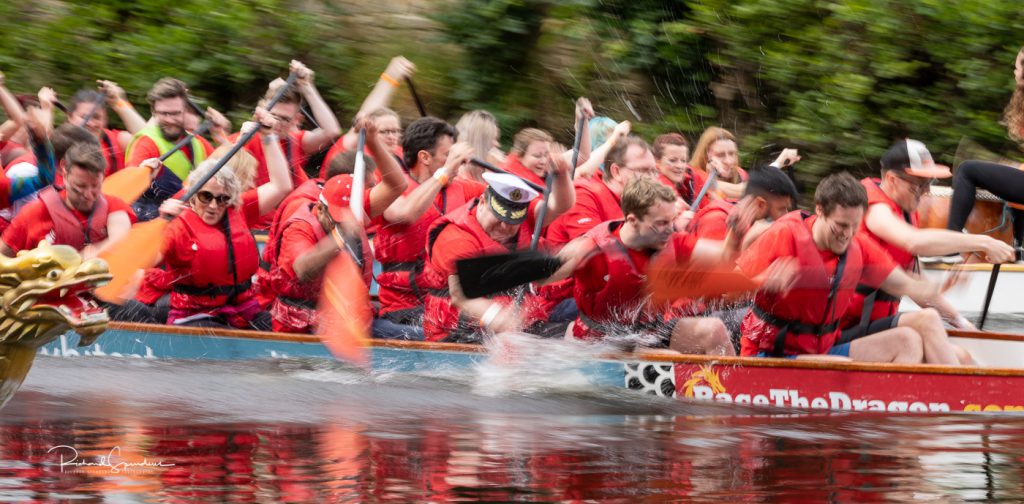 sport photography - sport photographer -colour image of dragon boat racing on the river aire at roberts park saltaire, a slow shutter speed was used together with panning to give a feel of the speed in this one the boats are all very close in the reave and there is lots of effort going into the paddling by all the crews