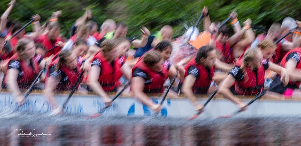 sport photography - sport photographer -colour image of dragon boat racing on the river aire at roberts park saltaire, a slow shutter speed was used together with panning to give a feel of the speed all the paddlers in the shot have they paddles synch and all pulling the water together
