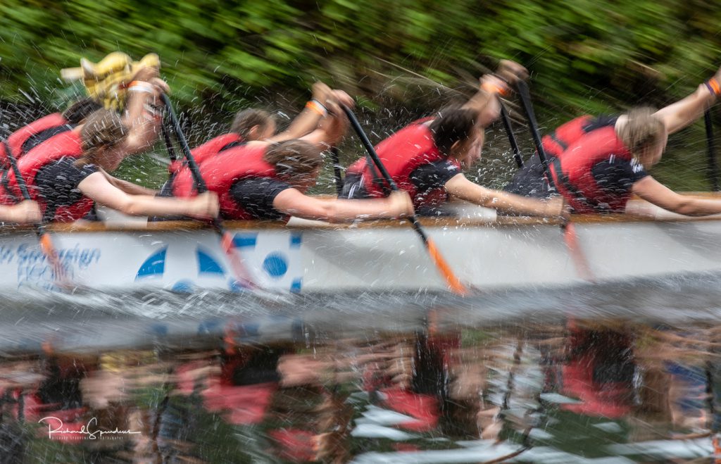 sport photography - sport photographer -colour image of dragon boat racing on the river aire at roberts park saltaire, a slow shutter speed was used together with panning to give a feel of the speed an on camera flash fired and froze the water droplets as all the crew reach forward to pull the paddle back towards them