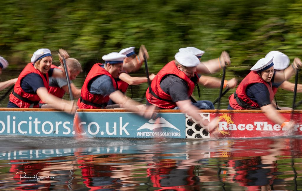 sport photography - sport photographer -colour image of dragon boat racing on the river aire at roberts park saltaire, a slow shutter speed was used together with panning to give a feel of the speed in this image on the paddlers has spotted the camera and is looking at it a smiling as they power past