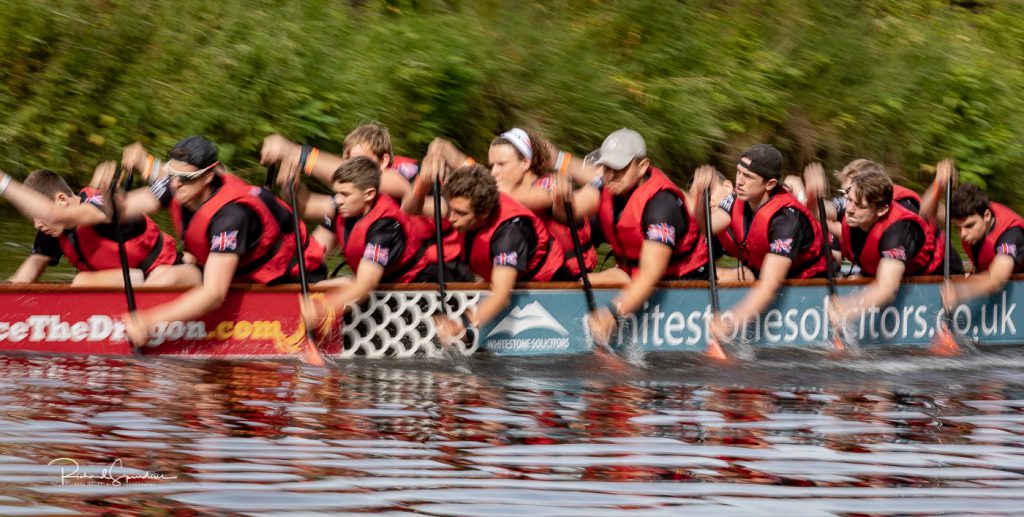 sport photography - sport photographer -colour image of dragon boat racing on the river aire at roberts park saltaire, slow shutter speed was used to help capture the feel of movement and speed in the image a male crew are all at the same point in the stroke with all their hands at the same point along the side of the boat