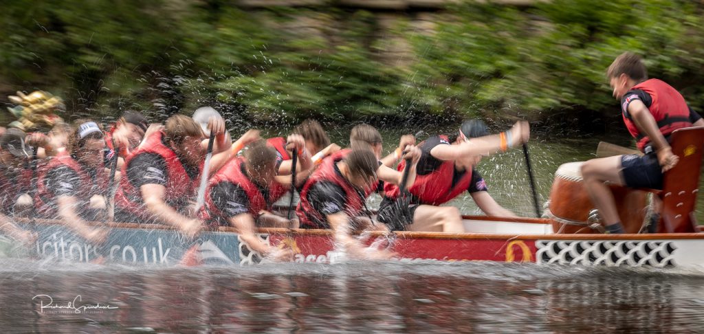 sport photography - sport photographer -colour image of dragon boat racing on the river aire at roberts park saltaire, a slow shutter speed was used together with panning to give a feel of the speed and a on camera flash was used to spot the water splashes as they paddle hard