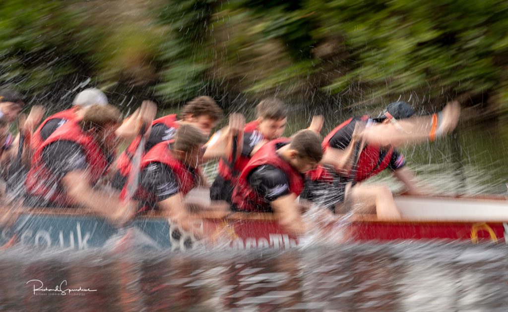 sport photography - sport photographer -colour image of dragon boat racing on the river aire at roberts park saltaire, a slow shutter speed was used together with panning to give a feel of the speed anone camera flash has captured all the water splash making it slightly more abstract type sports image
