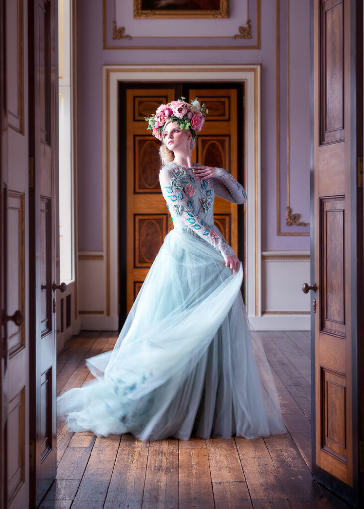 fashion photographer - fashion photography - image from a fashion shoot at wentworth woodhouse model wearing a pale blue full length ball gown with flowers and leave embroidery on the bodice and sleeves she is shot through the room doors