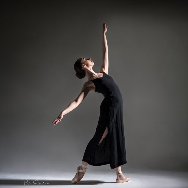 Dance Photographer - Dance photography - colour image of dancer Erica Mulkern facing into the light and reaching up to the sky and back with the other hand,she is wearing a long black dress