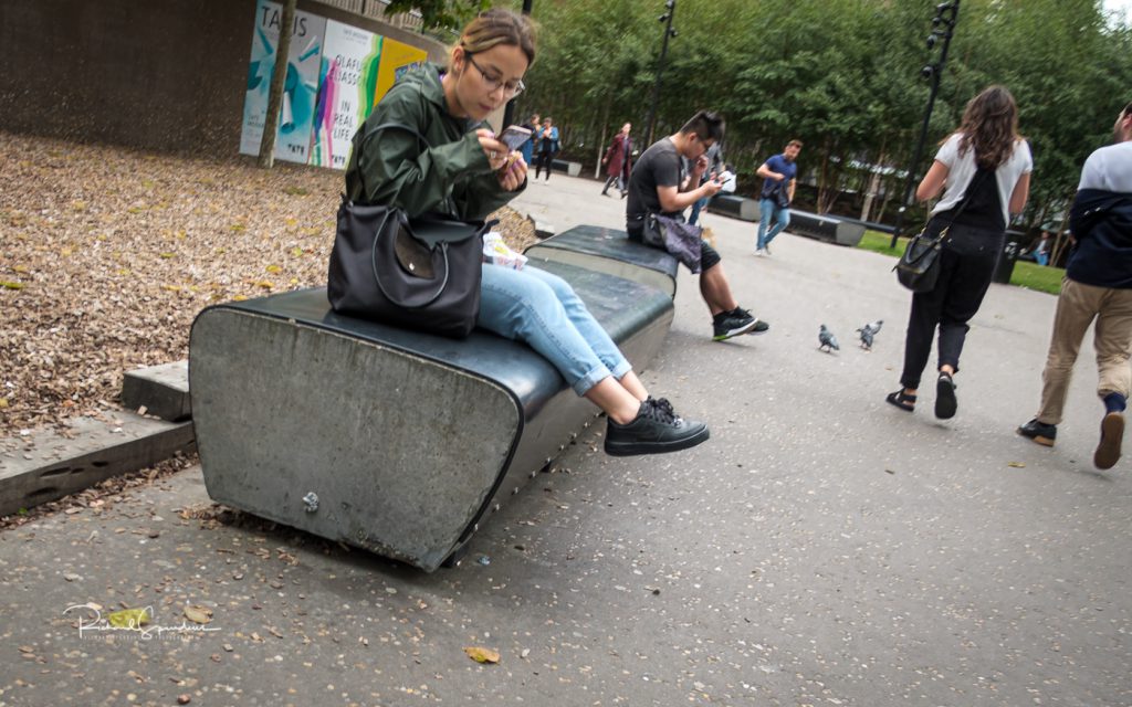 street photography - street photography - two people sat on a stone bench one at each end - both engaged with their phones