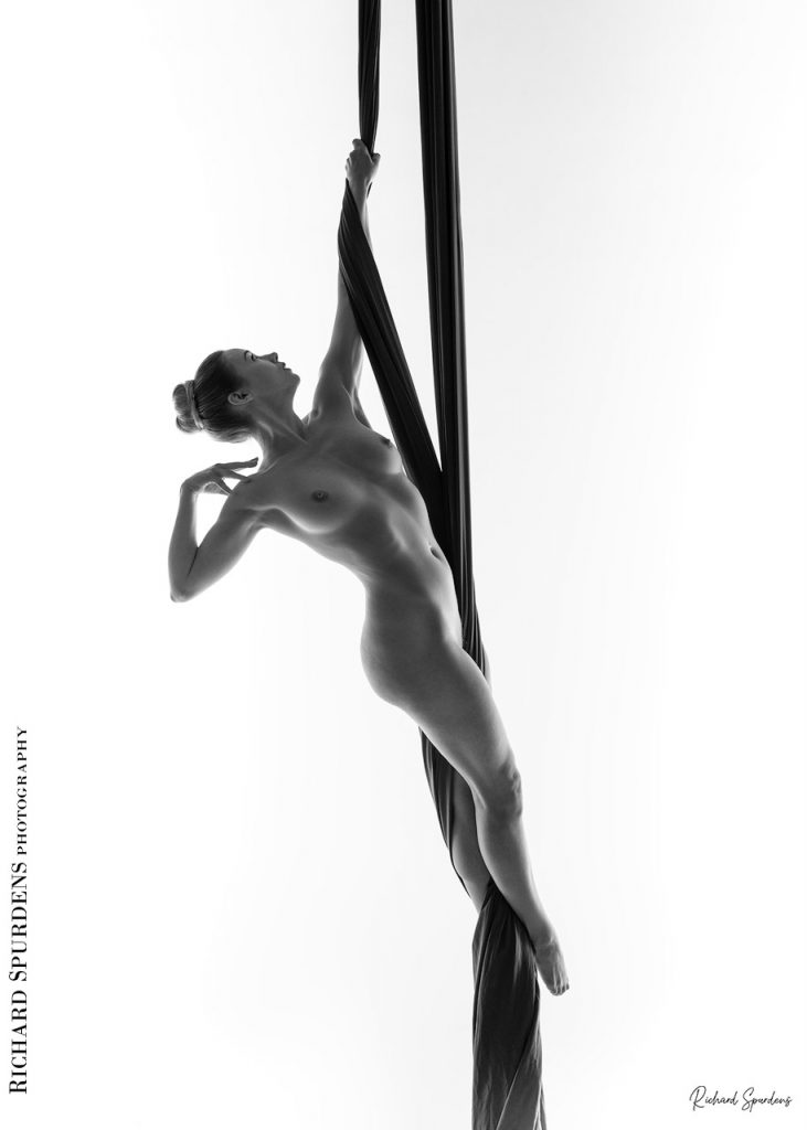 Aerial Arts photographer - Aerial Arts photography - Aerial silks photography - monochrome image of an aerialist Em using hanging silks to make strong hanging shapes just using arm and feet strenght