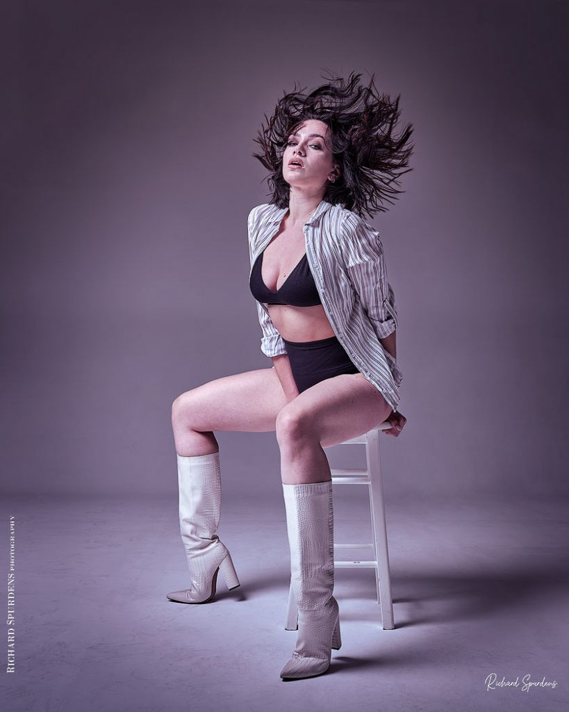 Fashion Photography - Fashion Photographer - model wearing white boots and striped shirt seated on a white stool flicking back here hair