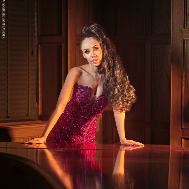 portrait photography - portrait photographer - image of model wearing a purple glitter dress leaning against a piano. looking towards the camera