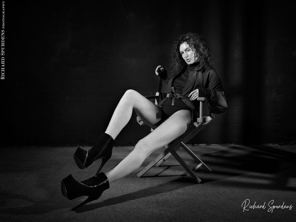 fashion photography fashion photographer - model seated on a directors chais stretching her long legs to show off the high heeled shoes