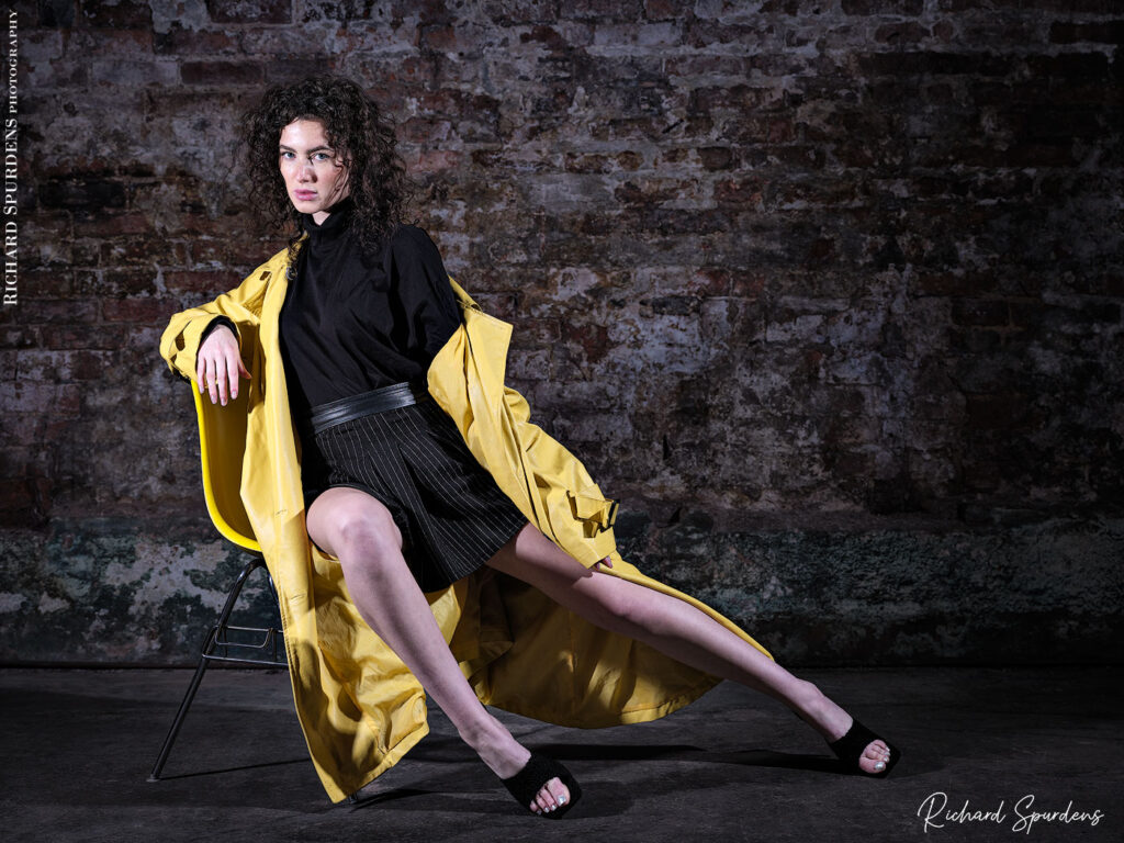 fashion photography fashion photographer - model ahsleigh ray lounging on a chair wearing a bright yellow mac and black skirt and top