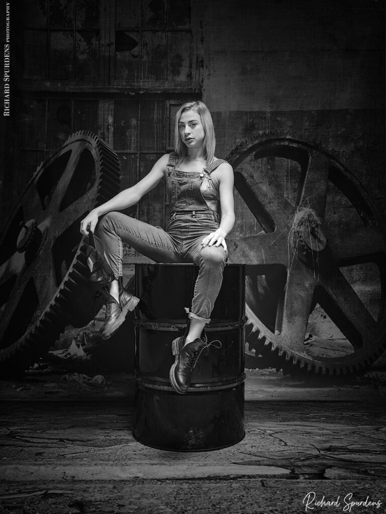 fashion photography - fashion photographer -Crystal fashion fun model wear dungrees posing on a oil drum, with industrial wheels in the background