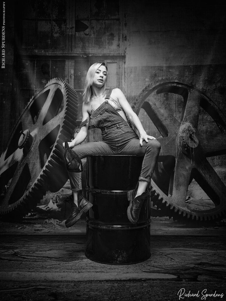 fashion photography - fashion photographer - Crystal fashion fun model wear dungrees posing on a oil drum, with industrial wheels in the background