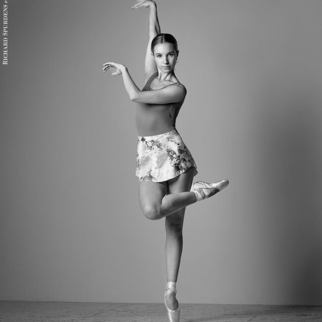 dance photographer - dance photography - dancer on a single pointe front leg bent across the front of the standing leg. Right arm across the body and left arm reaching behind.