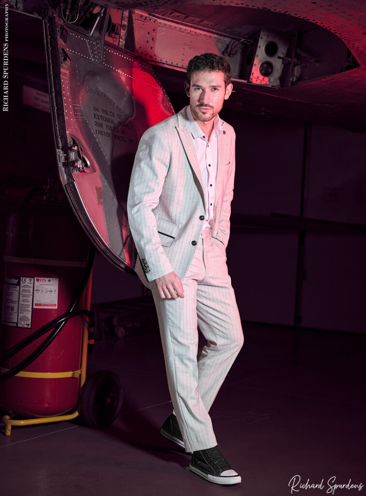 fashion photography fashion photographer - male model wearing a white pin strip suit posing amoung military aircraft.