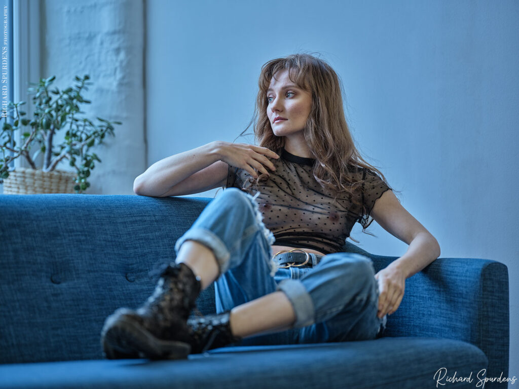 fashion photography fashion photographer - model wearing blue jeans seated on a blue settee looking out of the window